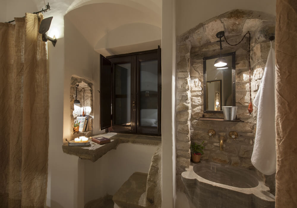 Interno di una celluzza con lavabo in pietra, specchio e candela alla finestra