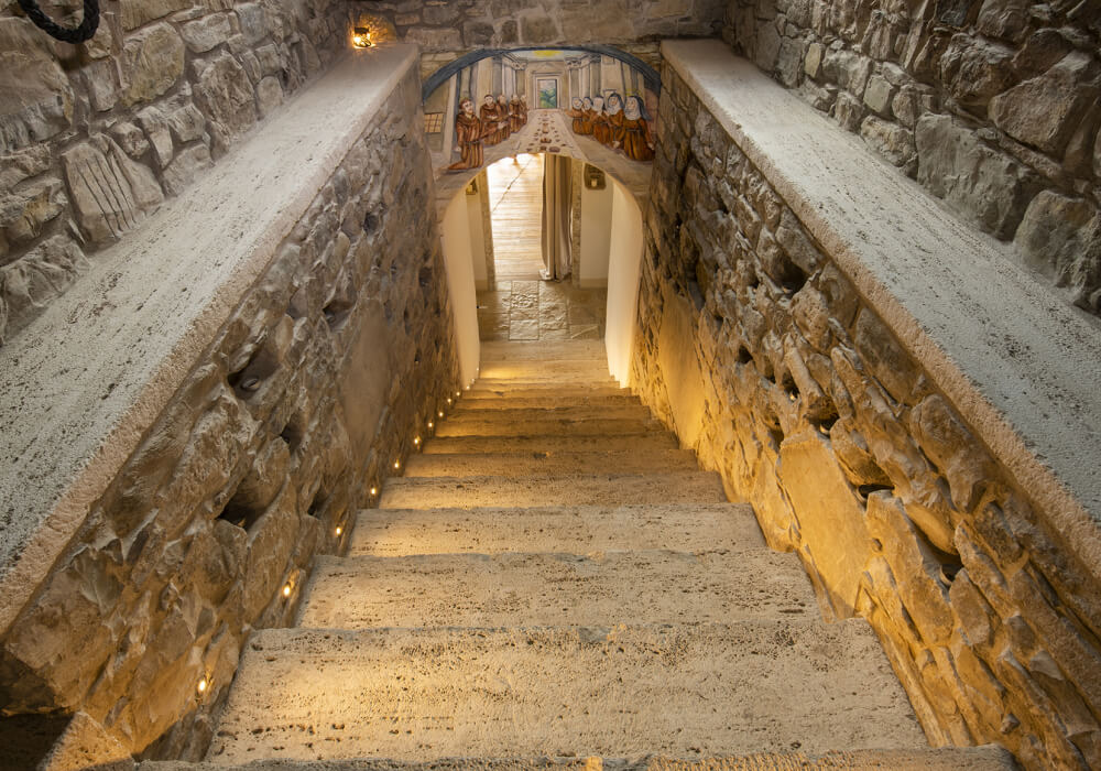 Stretto corridoio in pietra di Eremito con scalinata illuminata da luci a terra