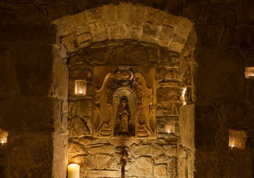 Nicchia in pietra illuminata con statua sacra e candele