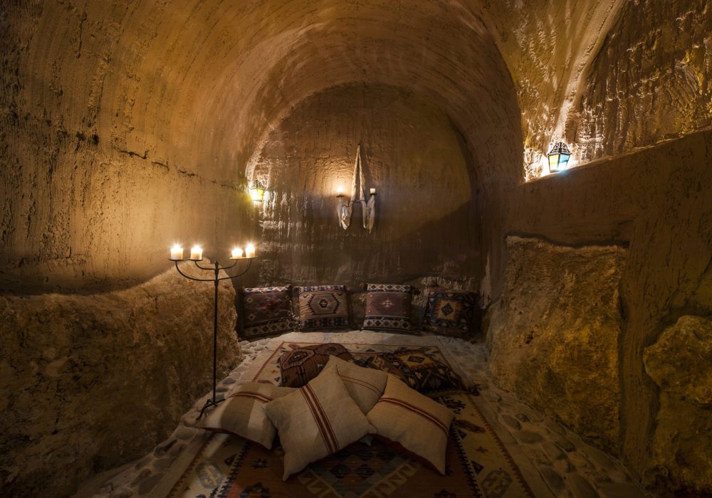 Sala voltata scavata nella roccia con lampadario a candele e cuscini