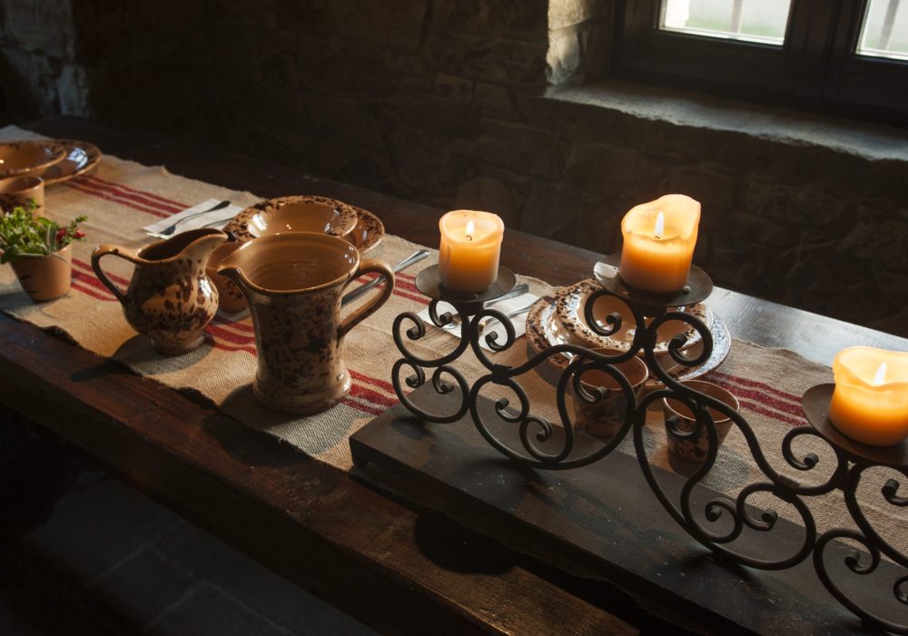 Tavolo del refettorio con candele accese e brocche in ceramica