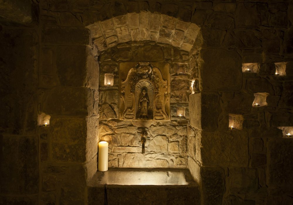 Nicchia in pietra illuminata con statua sacra e candela