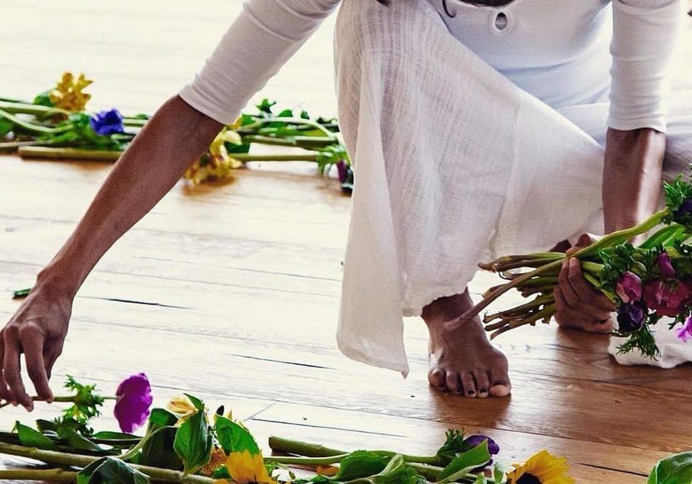 Ospite vestita di bianco che compone un mandala di fiori sul pavimento in pietra