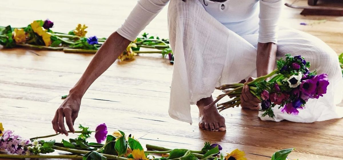 Ospite vestita di bianco che compone un mandala di fiori sul pavimento in pietra