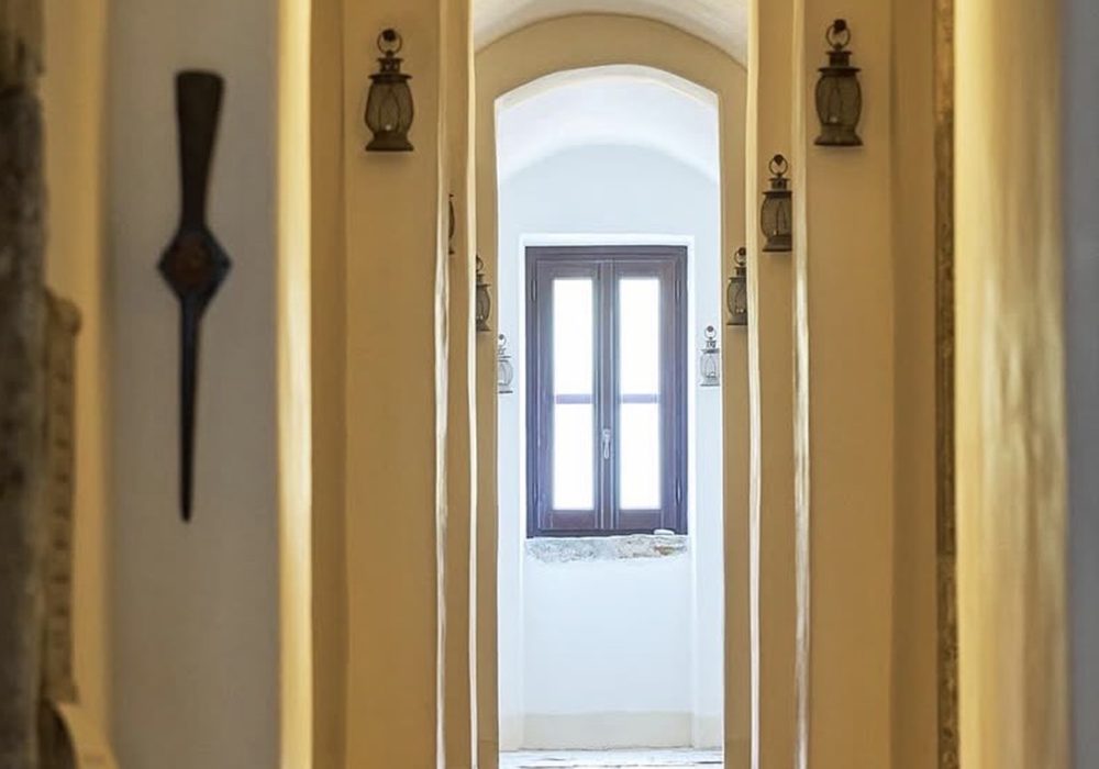 Corridoio di Eremito con lanterne in ferro alle pareti e la finestra in fondo