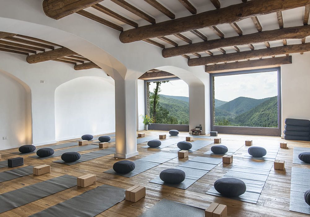 Sala yoga con travi a vista, cuscini da meditazione e vista sui boschi