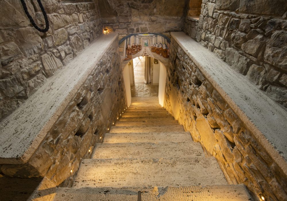 Scala in pietra illuminata da luci a terra che sale verso le celluzze