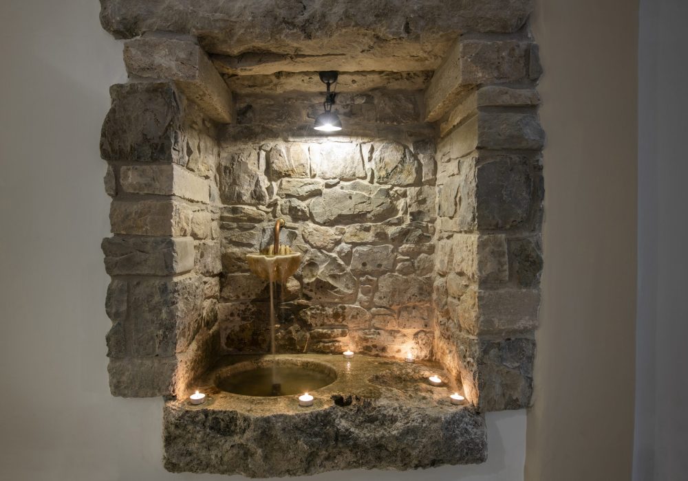 Fontana in ottone incassata nella parete in pietra tra le candele