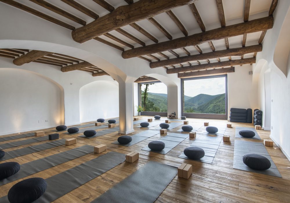 Sala yoga con travi a vista, cuscini da meditazione e vista sulla valle